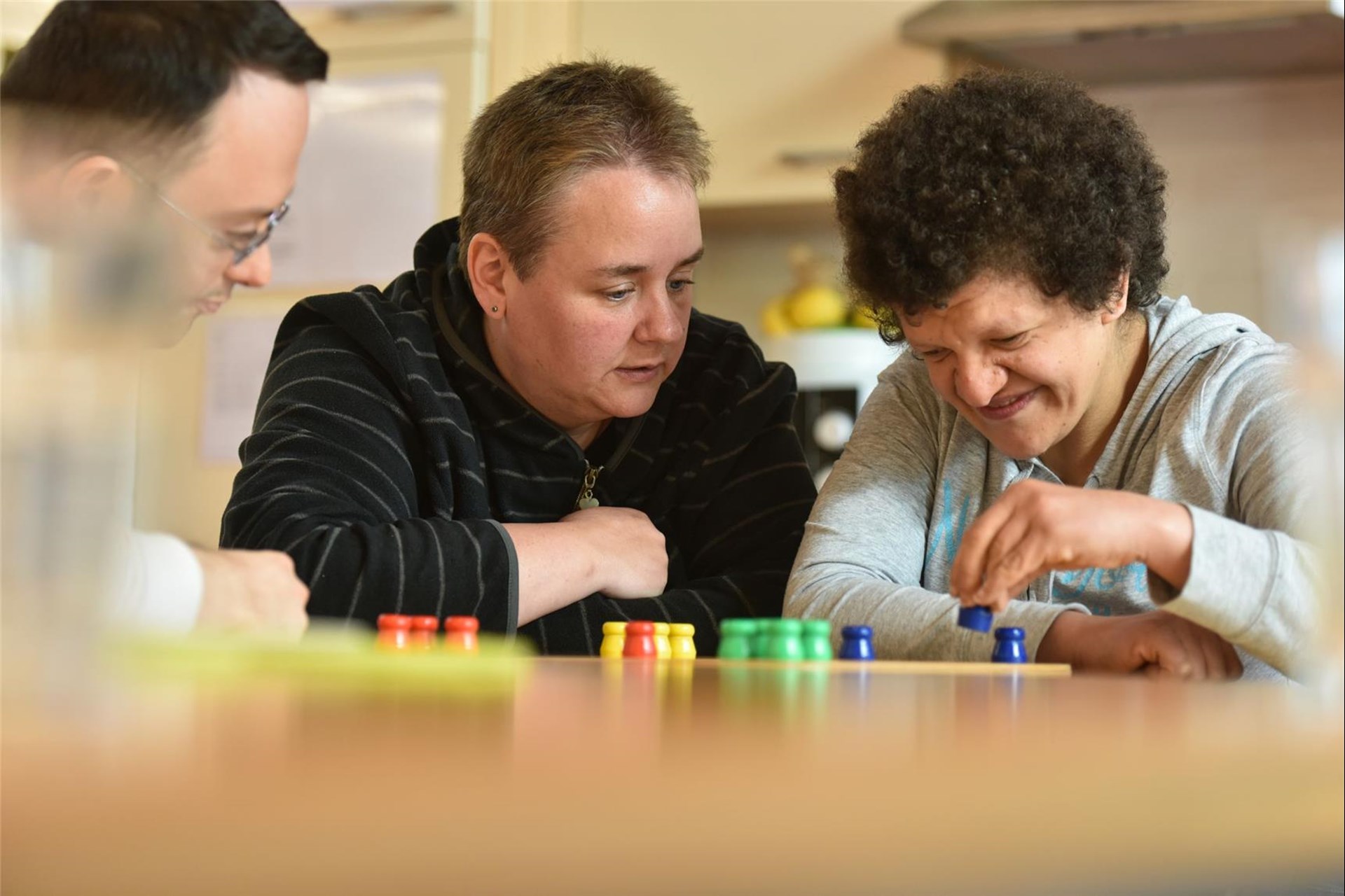 Betreuerin spielt mit zwei Menschen mit Behinderung ein Brettspiel